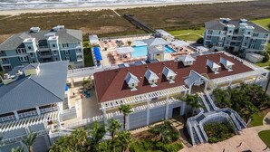 An aerial view of a beachfront hotel with multiple buildings, a swimming pool, and a pier extending into the ocean.