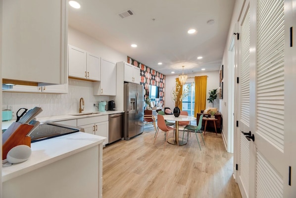 A modern kitchen with white cabinetry, a stainless steel refrigerator, and a dining area with a round table and colorful chairs.