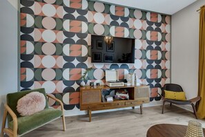 A living room with a geometric patterned wall, a television, a wooden console, and two chairs.