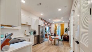 A modern kitchen with white cabinets, a stainless steel refrigerator, and a dining area with a round table and chairs.