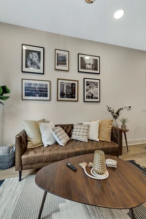 A living room with a brown leather sofa, a round wooden coffee table, and framed pictures on the wall.
