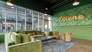 A modern lounge area with green upholstered sofas, a patterned rug, and a wall with the word 'Dolene' illuminated.