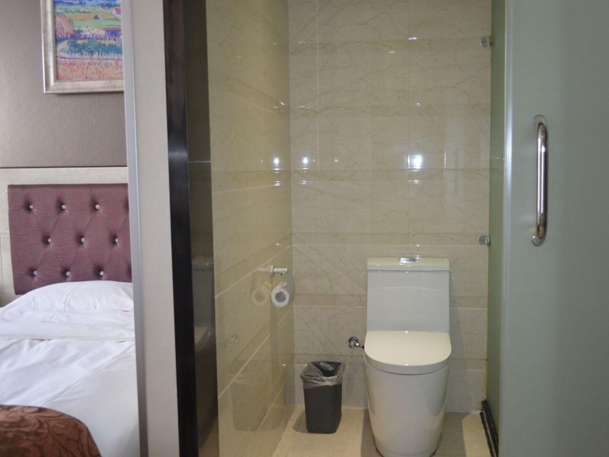 A hotel bathroom with a glass shower enclosure, a toilet, and a trash bin.