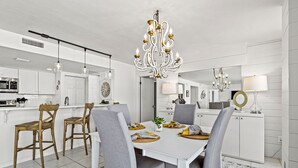A modern kitchen with white cabinetry, a dining area with grey upholstered chairs, and a chandelier.