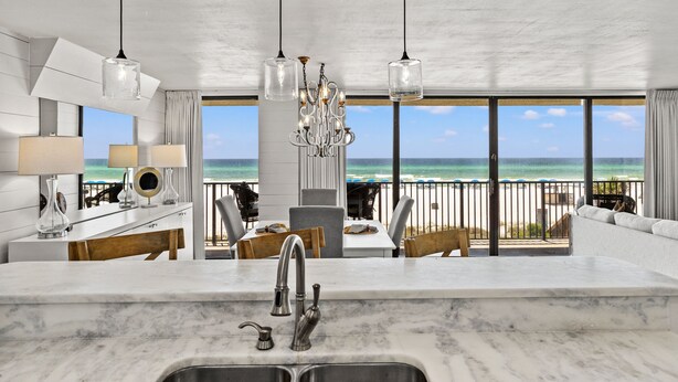 A modern kitchen with a large island, a view of the beach, and a dining area with outdoor seating.