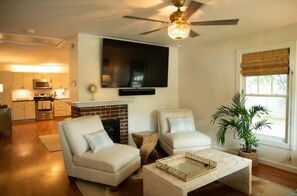 A living room with two sofas, a coffee table, a TV mounted on the wall, a fireplace, and a ceiling fan.