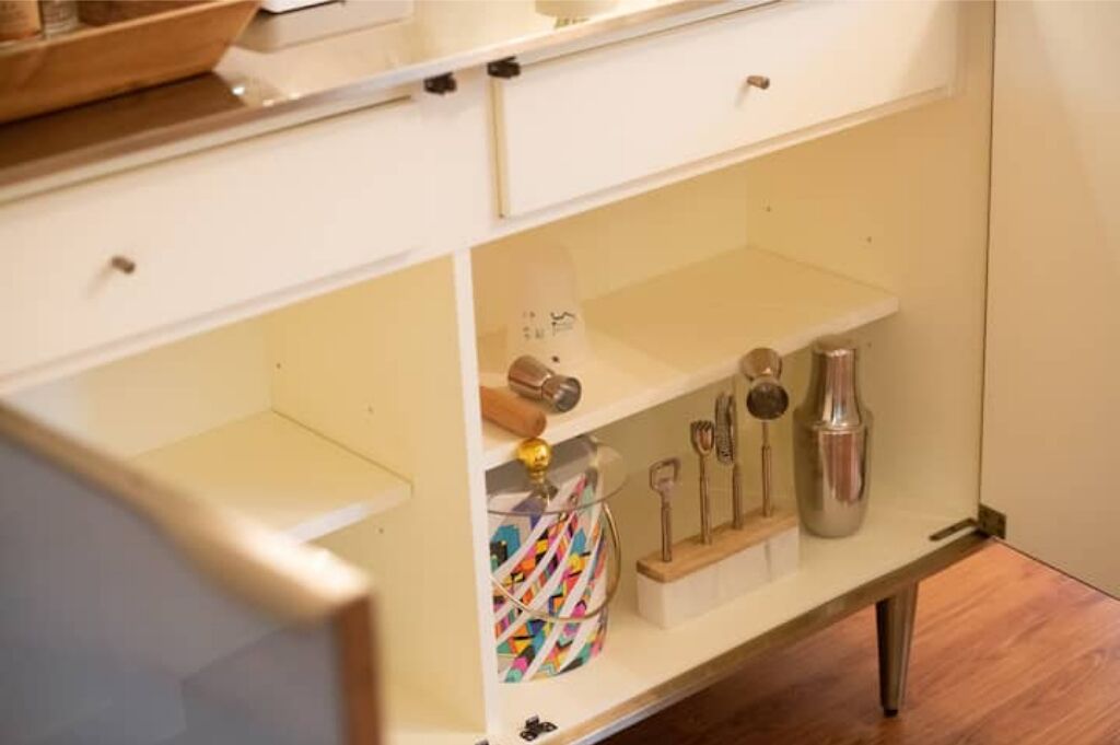 A kitchen with white cabinets, a wooden countertop, and a shelf with kitchen utensils and a decorative item.