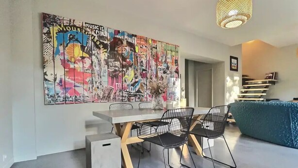Un soggiorno moderno con zona pranzo, caratterizzato da una grande opera d'arte astratta appesa al muro, un tavolo da pranzo contemporaneo e sedie nere dalla struttura a filo.
