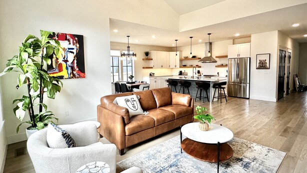 A modern living room with a brown leather sofa, a white armchair, and a round coffee table. There is a dining area with a kitchen in the background. - New Luxury House, walk to Asheville’s best restaurants, pubs breweries and shops (Asheville)