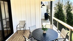 A covered patio with a round table and chairs, wooden flooring, and a view of the outdoors. - New Luxury House, walk to Asheville’s best restaurants, pubs breweries and shops (Asheville)