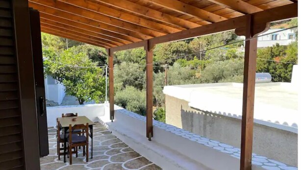 A covered patio with a stone floor, wooden furniture, and a view of greenery and buildings. - Nionas Cheerful House (Piso Meria)