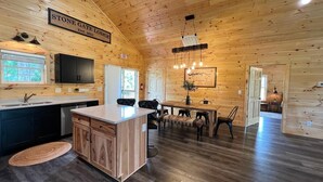 Een ruim interieur van een lodge met houten inrichting, een keukenhoek, een eethoek en een bord met de naam en het vestigingsjaar.