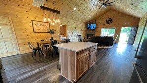 Een ruime keuken met een centraal eiland, houten wanden en een eethoek met stoelen en een tafel.