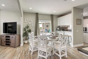Un coin repas avec une table ronde, des chaises blanches, une plante en pot et un téléviseur posé sur un meuble.