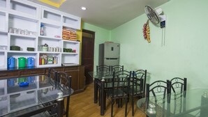 A compact kitchen with a dining area, featuring a refrigerator, shelves with kitchenware, and a dining table with chairs. - OYO 161 Ram Janaki Hotel (Kathmandu)