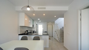 A modern kitchen with a dining area, white walls, and a staircase leading to another level. - Apartamento Calma (Mar de Pulpi) (San Juan de los terreros)