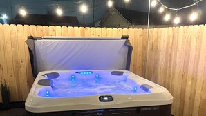 Un bain à remous doté d’un panneau de commande, entouré d’une clôture en bois, et une guirlande lumineuse au-dessus.