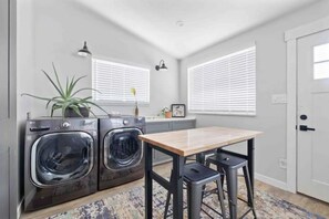 Une cuisine compacte équipée de deux lave-linge à chargement frontal, d’une table en bois et de tabourets de bar.