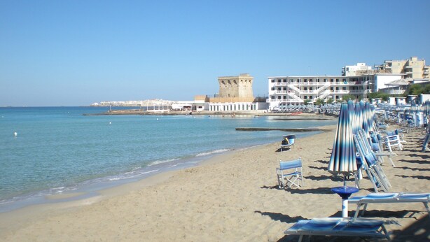 A beach with clear blue water, a sandy shore, and a row of beach chairs and umbrellas. - Lido San Giovanni (Gallipoli)