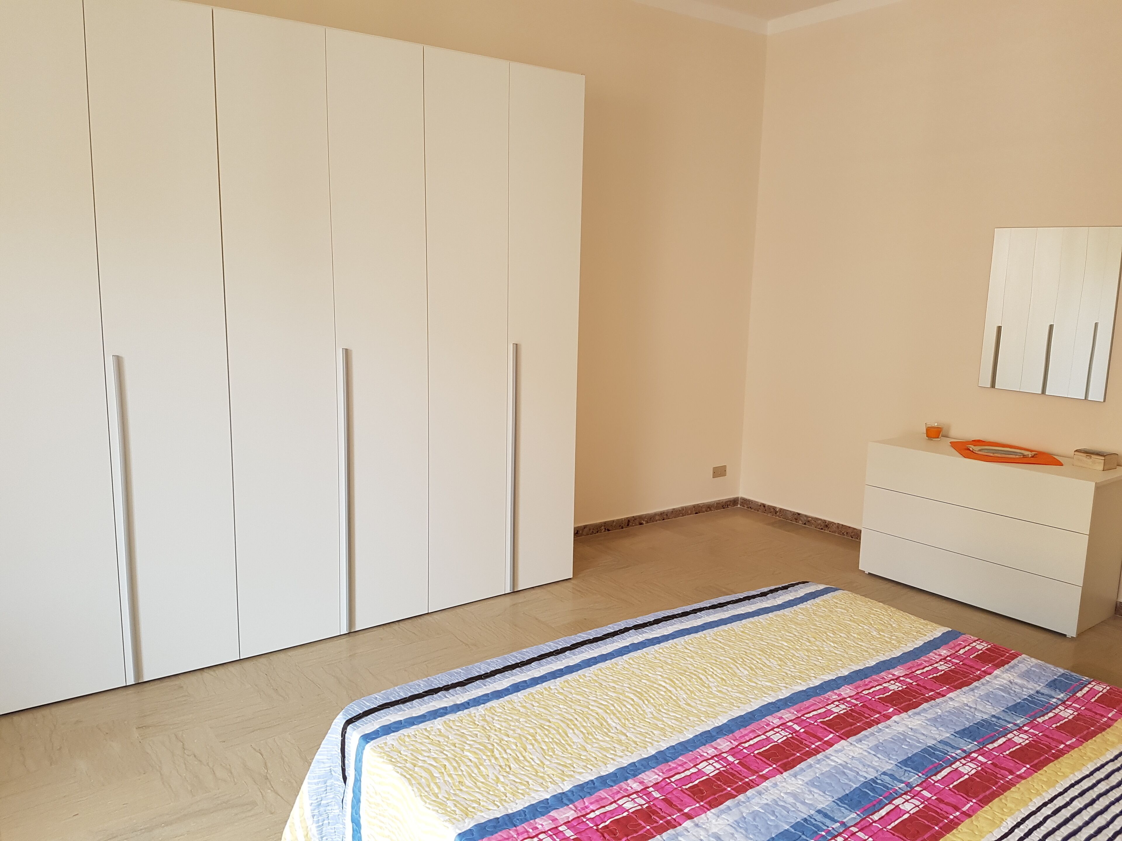 Een slaapkamer met een grote garderobe, een nachtkastje met spiegel en een kleurrijk beddegoed.
