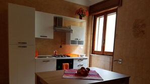A kitchen with white cabinets, a gas stove, and a window with curtains. - Lido San Giovanni (Gallipoli)