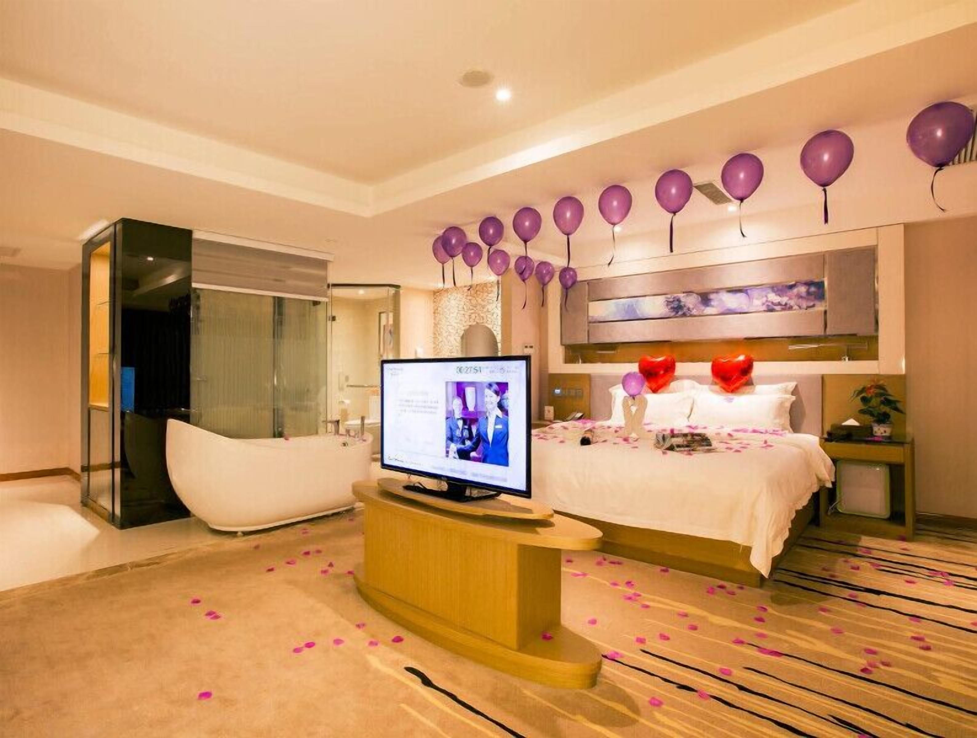 A modern hotel room with a large bed, a bathtub, and a television.