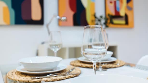 Une table à manger avec des assiettes blanches, des verres transparents et des sets de table en fibres tressées.