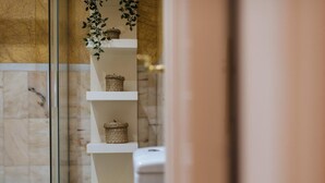 Une salle de bain avec un mur en marbre, une douche en verre et une étagère blanche agrémentée de paniers en osier.
