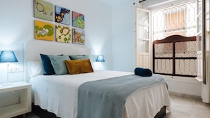 Une chambre à coucher avec un lit, deux tables de chevet, une fenêtre donnant sur un beau paysage et des œuvres d’art accrochées au mur.