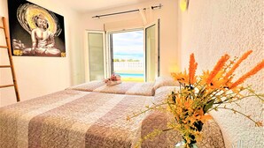 Une chambre avec deux lits, un tableau représentant un Bouddha, une fenêtre donnant sur la plage et un vase rempli de fleurs.