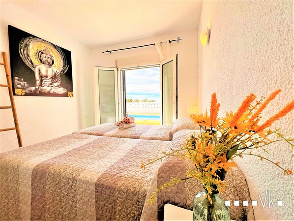 A bedroom with two beds, a painting of a Buddha, a window with a view of the beach, and a vase with flowers. - Villa CHAMPY in Moraira – Sea views, private pool, 2 bedrooms, air conditioning and Wi-Fi (Moraira)