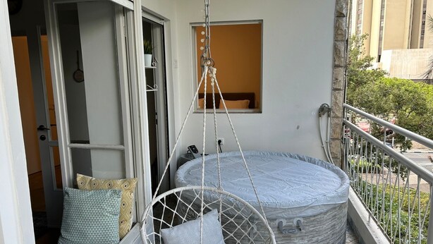 Un balcón con una silla colgante y un colchón redondo.