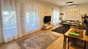 Amplia sala de estar con piso de madera, una mesa de comedor con sillas, un televisor de pantalla plana y un sofá.