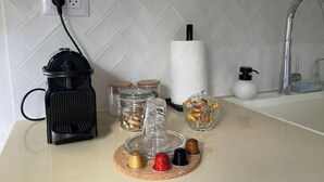Una encimera de cocina con una cafetera, frascos, un recipiente de vidrio y un rollo de toallas de papel.