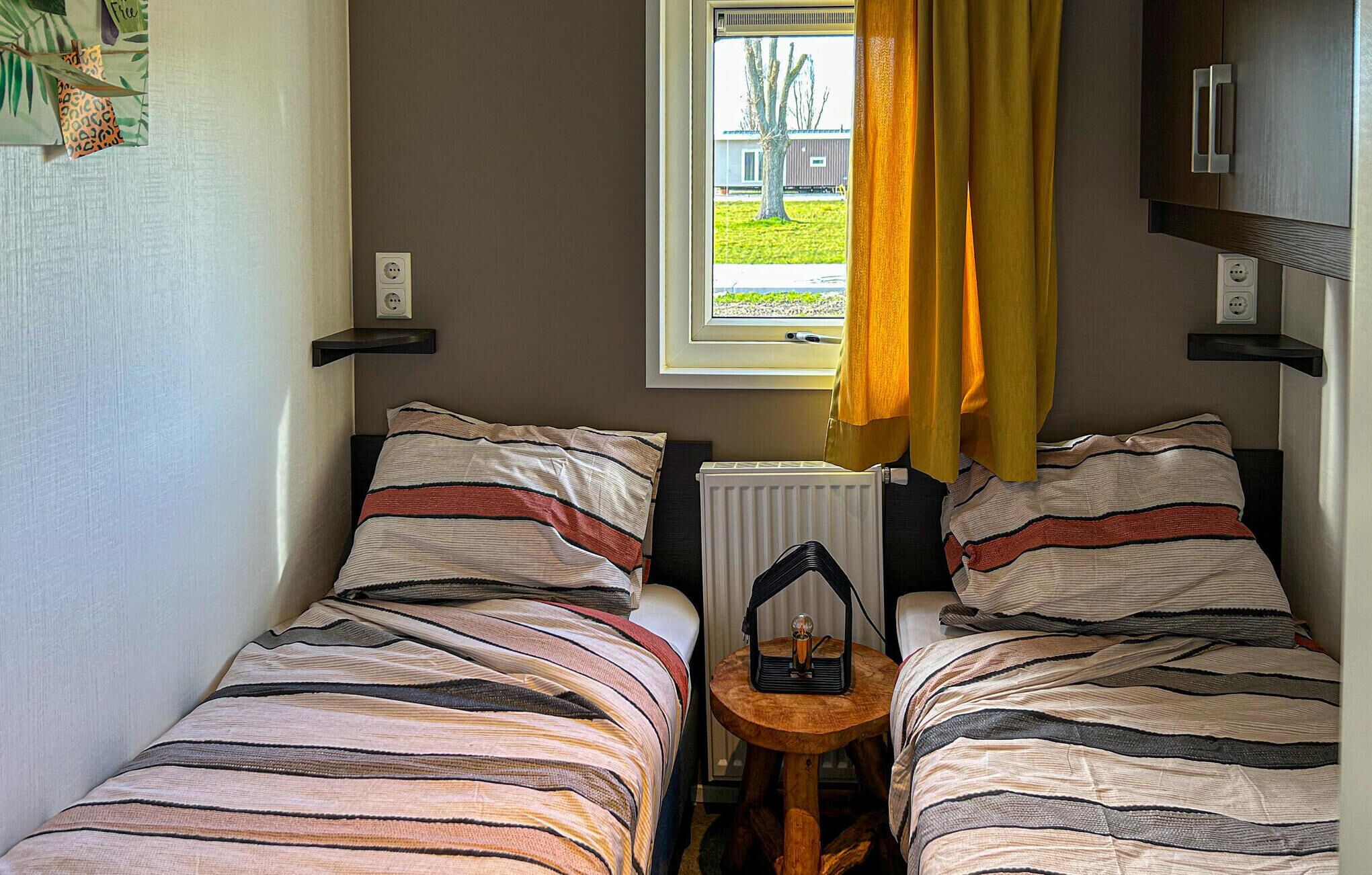 Een kleine, knusse kamer met twee bedden, een raam met gordijnen en een radiator.
