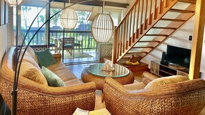 Un vaste espace de vie agrémenté de meubles en osier, d’une table basse en verre et d’un escalier en bois.