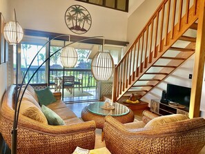 A spacious living area with wicker furniture, a glass coffee table, and a wooden staircase. - 2BR/1BA Condo: Amazing Views, Pool, Lanai, and best Sunsets (Maunaloa)
