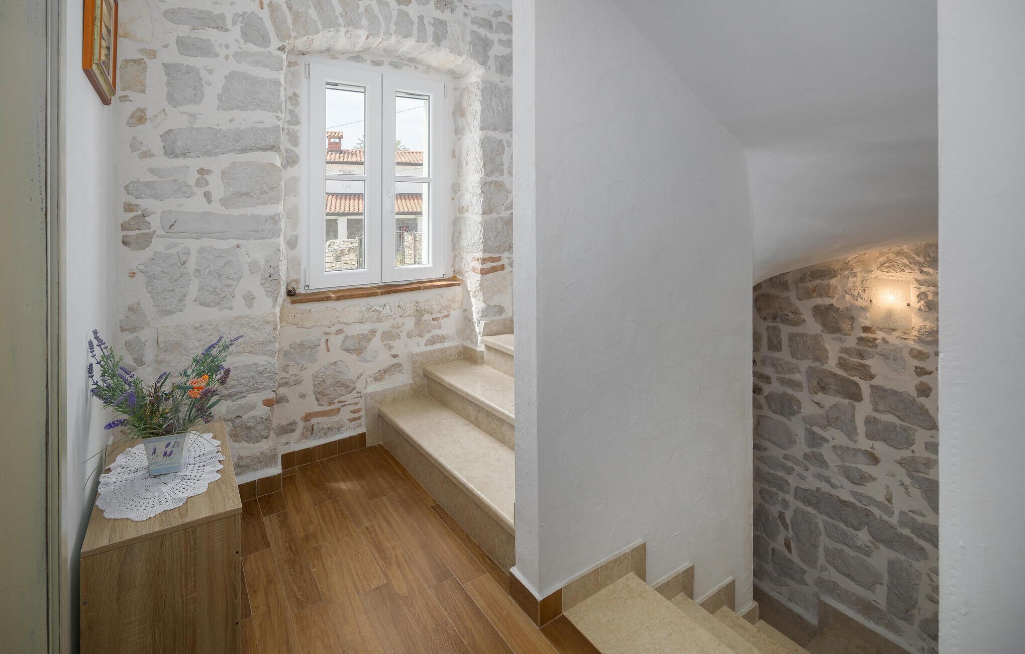 Eine Treppe mit Steinwänden, Holzboden und einem Fenster mit Blick auf Gebäude.