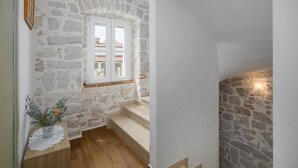 Un escalier avec des murs en pierre, un plancher en bois et une fenêtre donnant sur les bâtiments environnants.