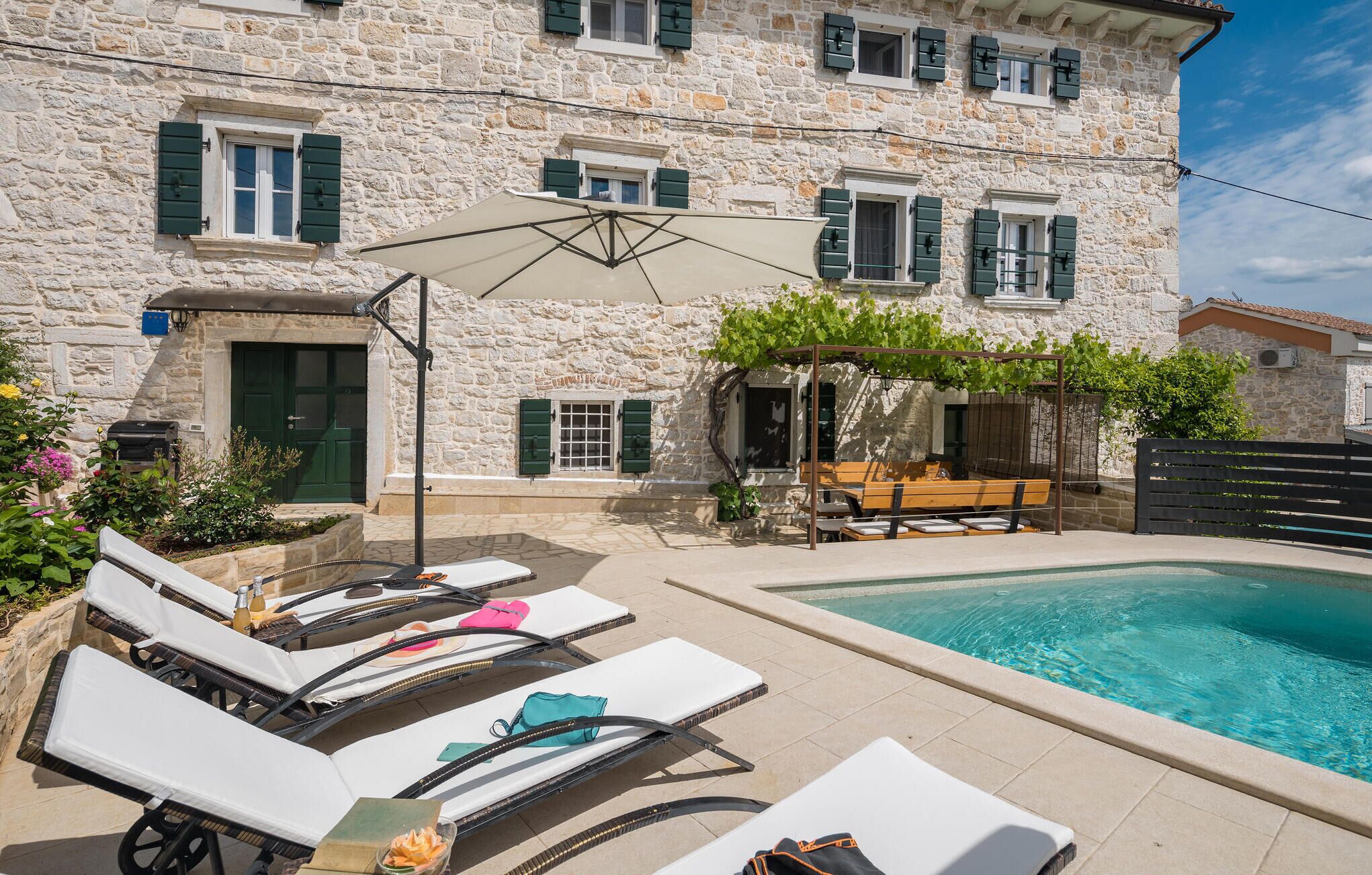 Ein Gebäude aus Stein mit Pool, Sitzgelegenheiten im Freien und Liegestühlen.