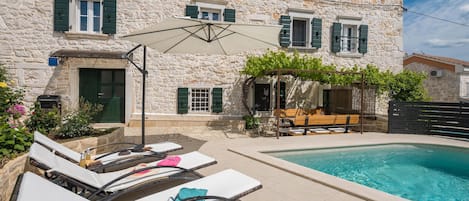 Ein Gebäude aus Stein mit Pool, Sitzgelegenheiten im Freien und Liegestühlen.