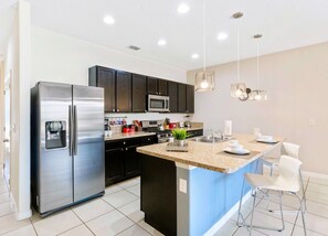 A modern kitchen with stainless steel appliances, dark cabinets, and a central island with seating.