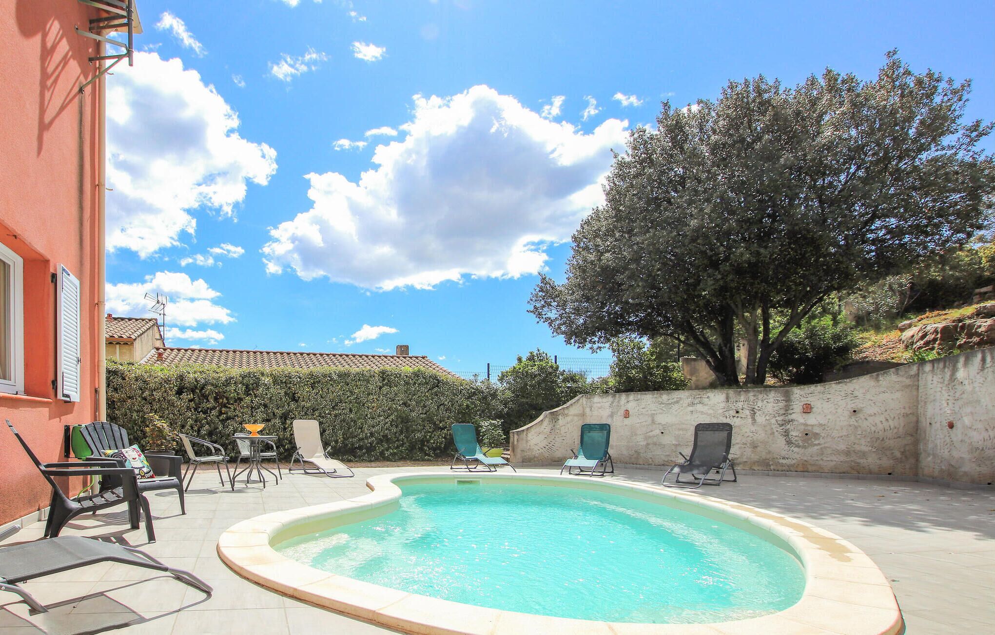 A swimming pool with lounge chairs, a red building, and a tree in the background.