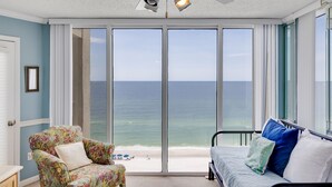 Ein Schlafzimmer mit einem großen Schiebeglasfenster mit Blick auf einen Strand, einem Deckenventilator und einem Bett mit Kissen.