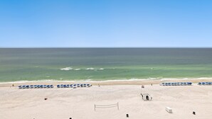 Ein Strand mit Volleyballnetz, blauen Sonnenschirmen und blauem Himmel.