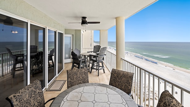 Ein Balkon mit Tisch und Stühlen, einem Deckenventilator und Blick auf den Strand.