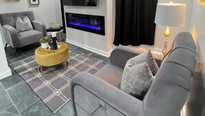 Uma sala de estar moderna com um sofá cinzento, uma mesa de centro redonda, uma TV de tela plana na parede e um tapete estampado.