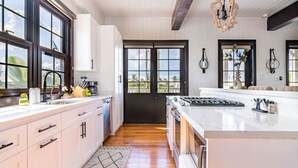 Een moderne keuken met witte kasten, een groot eiland en uitzicht door een donkere deur.