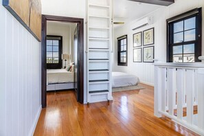 Een kamer met een bed, een witte ladder, een witte leuning en botanische prints in lijsten aan de muur.