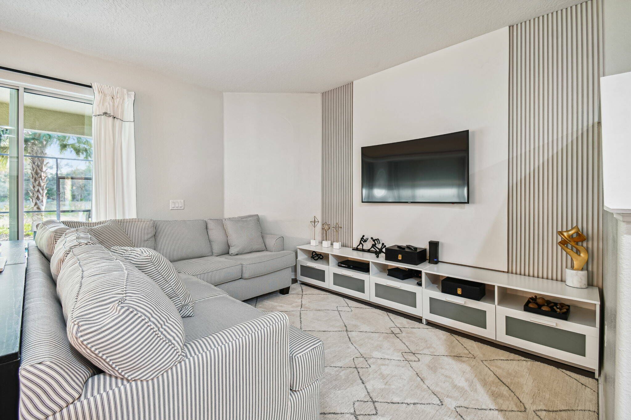 A modern living room with a sectional sofa, a flat-screen TV mounted on the wall, and a white entertainment unit with storage.